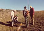 Scientists examining soil samples at soil surface with ecotone in background